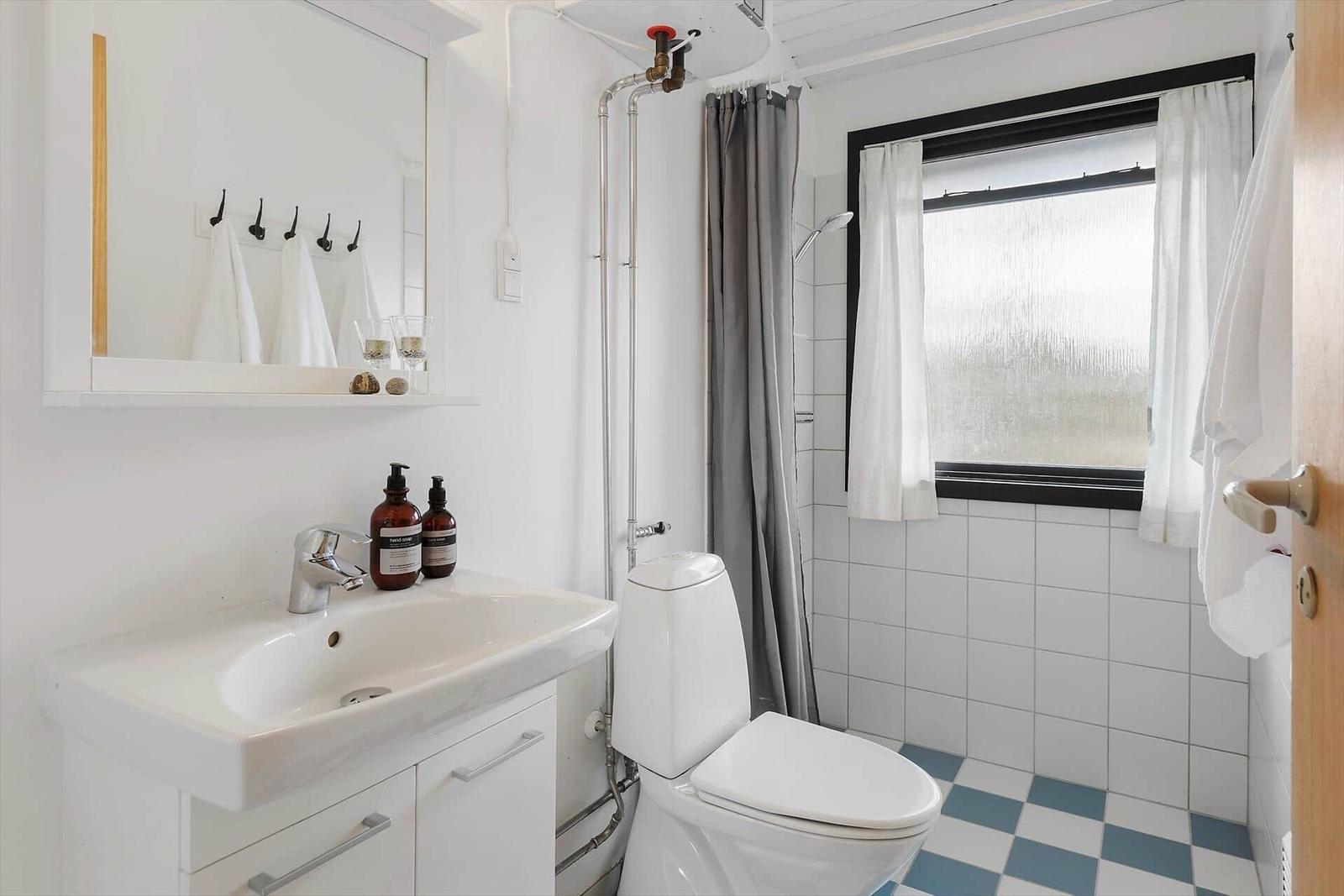 Badezimmer mit Toilette, Waschbecken und Dusche. Fenster mit weißen Vorhängen.