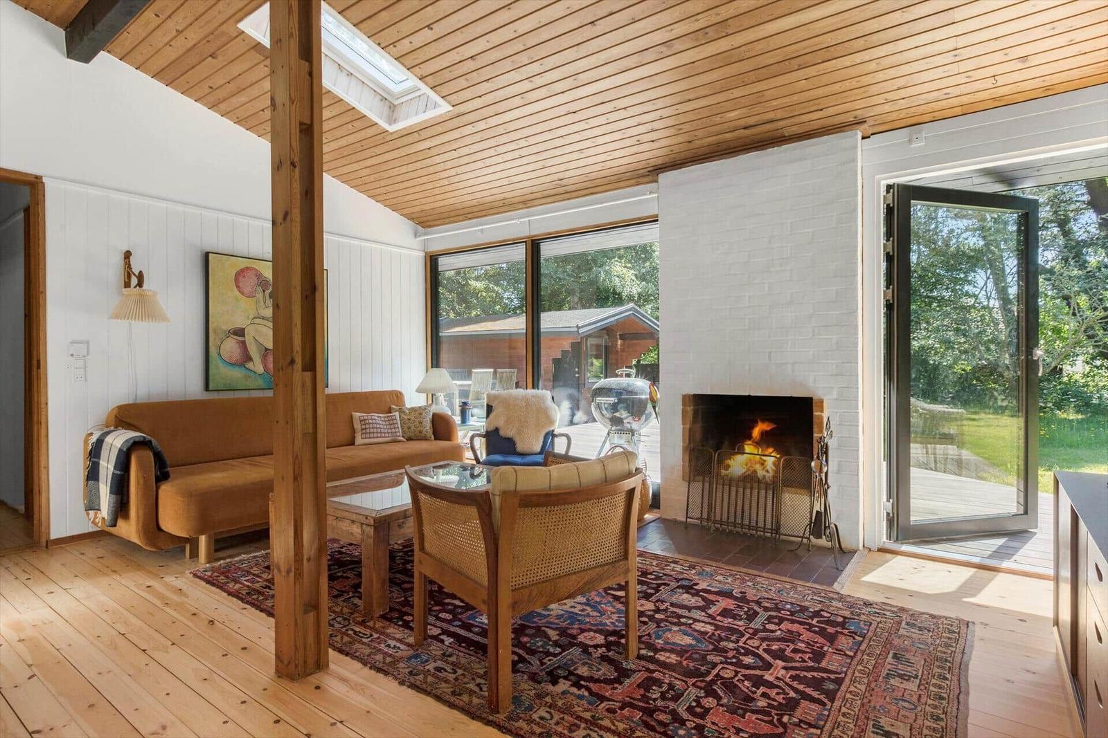 Wohnzimmer mit Kamin, Holzdecke und Glasfront zur Terrasse.