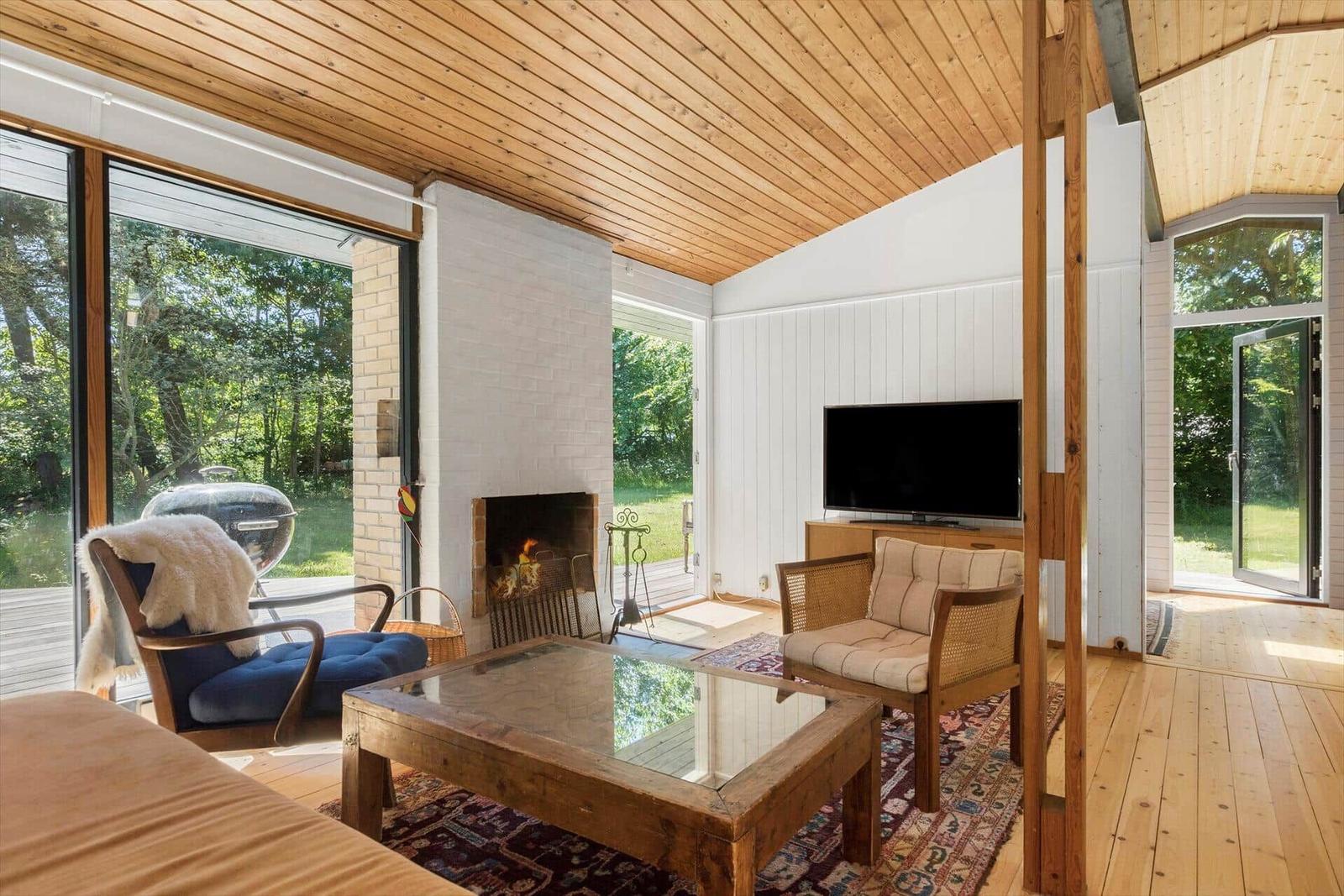 Wohnzimmer mit Kamin, Fernseher und großem Fensterblick auf Garten.