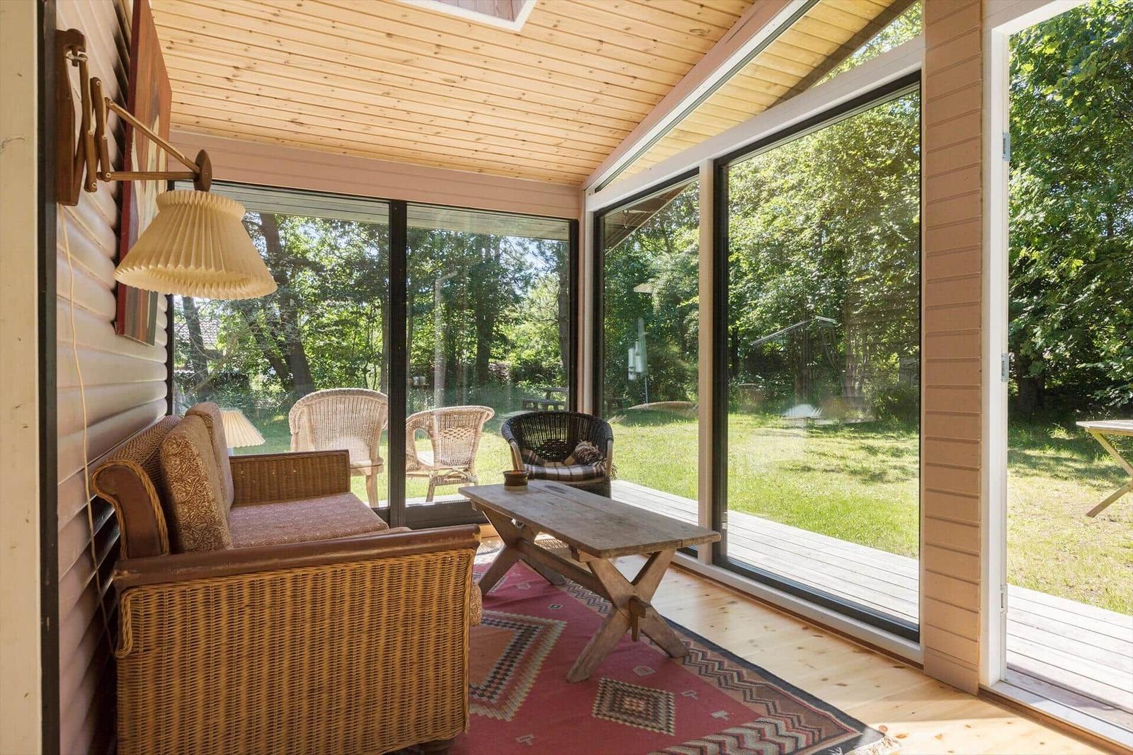 Wohnbereich mit Sitzgruppe, Tisch und Blick auf Garten durch große Fenster.