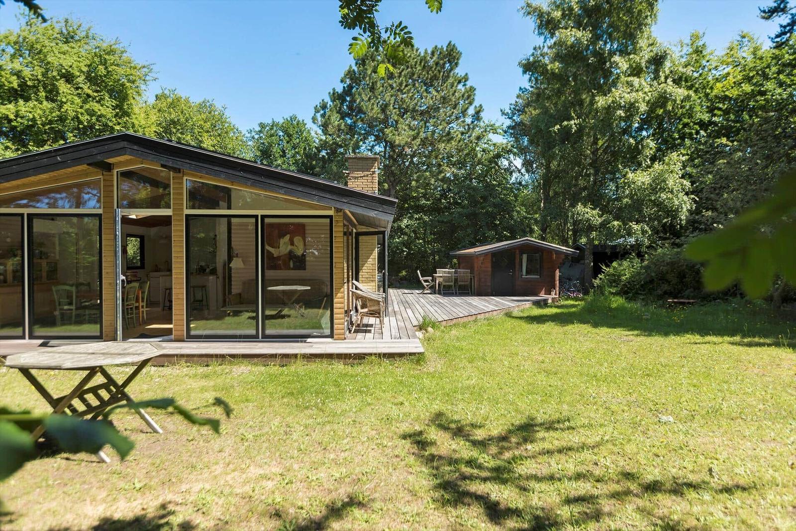 Moderne Holzhütte mit großem Glasbereich und Terrasse im Grünen.