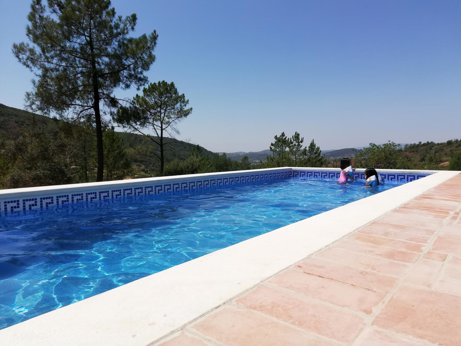 Pool mit Blick auf bewaldete Hügel. Zwei Kinder schwimmen im Wasser.