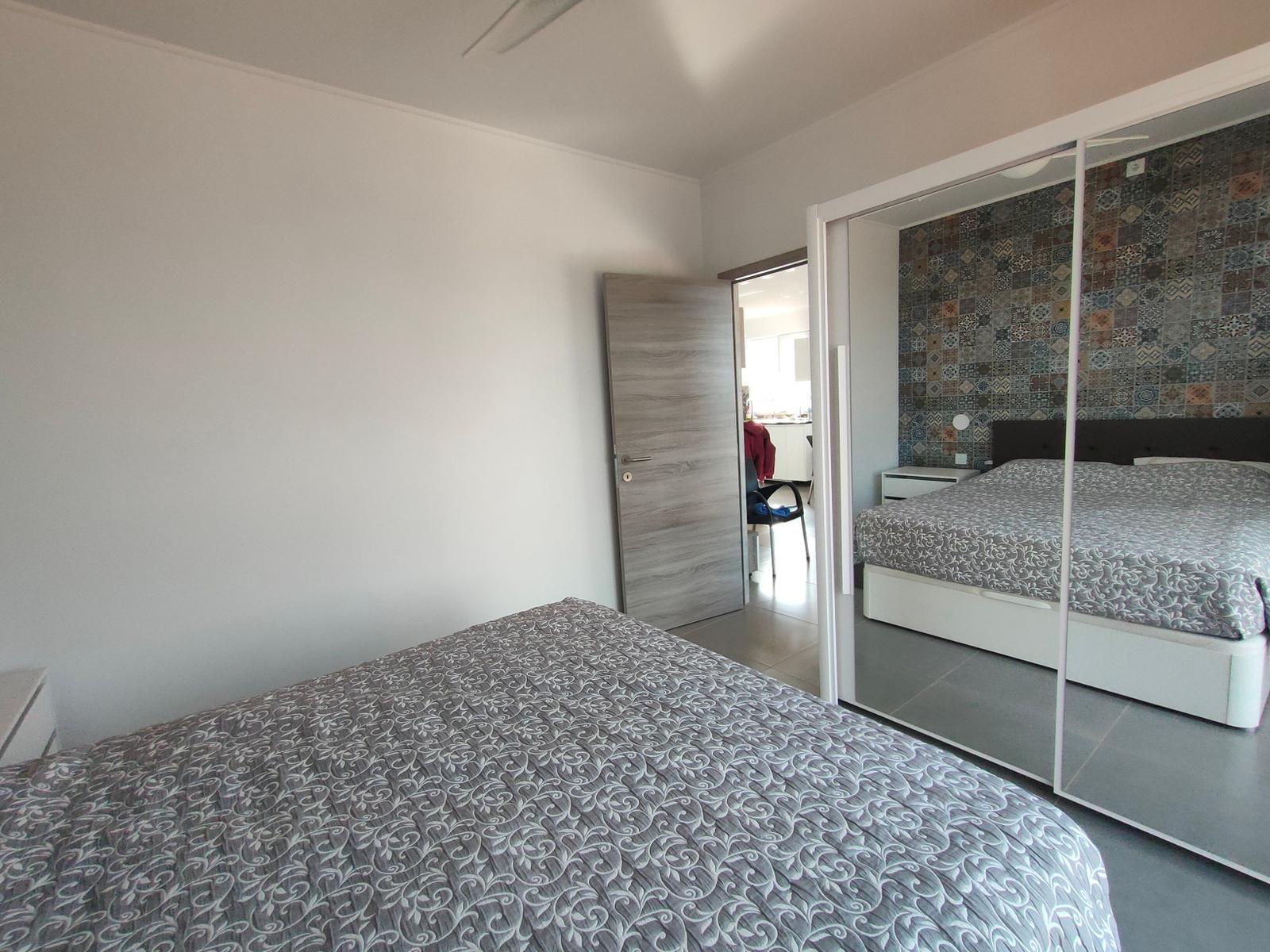 Schlafzimmer mit Bett, Spiegelschrank und Tür zum Flur.