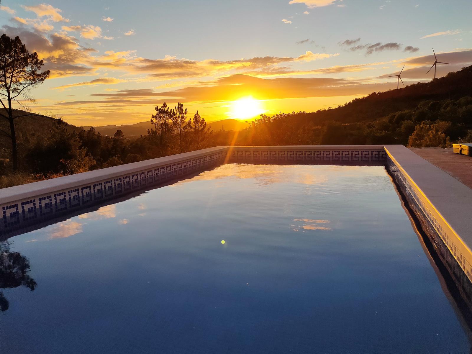 Pool mit Blick auf Sonnenuntergang und Hügel mit Windkraftanlagen.