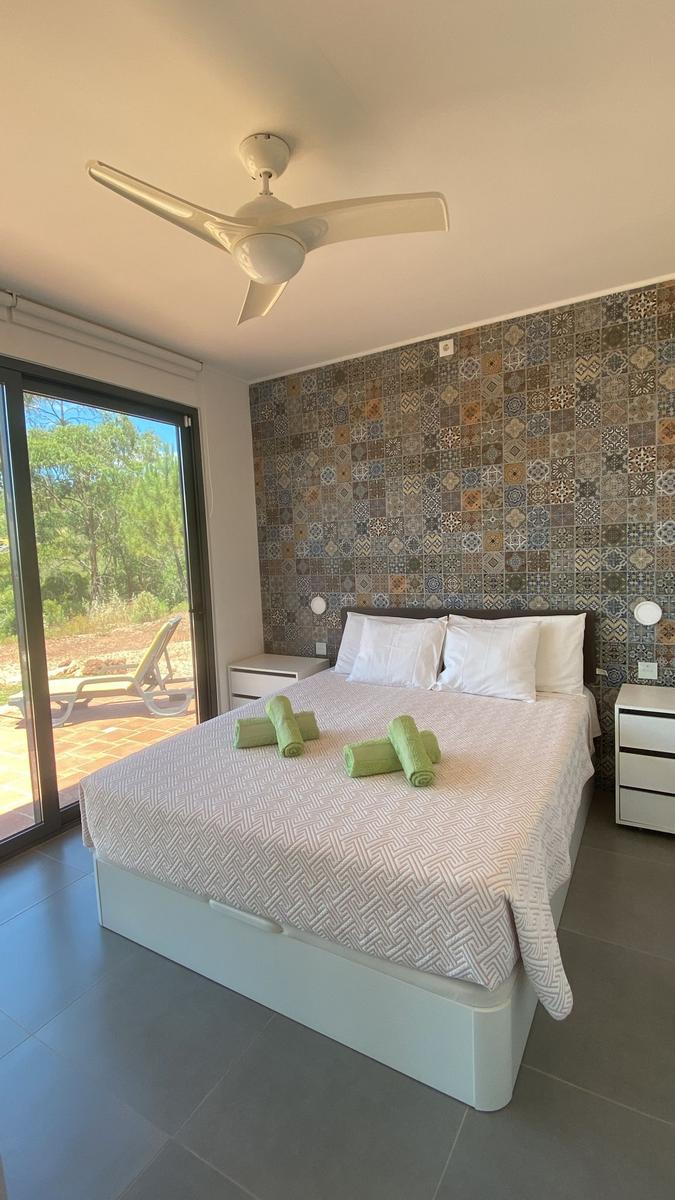 Schlafzimmer mit Bett, Decke, Nachttischen und Flügeltür zum Balkon.
