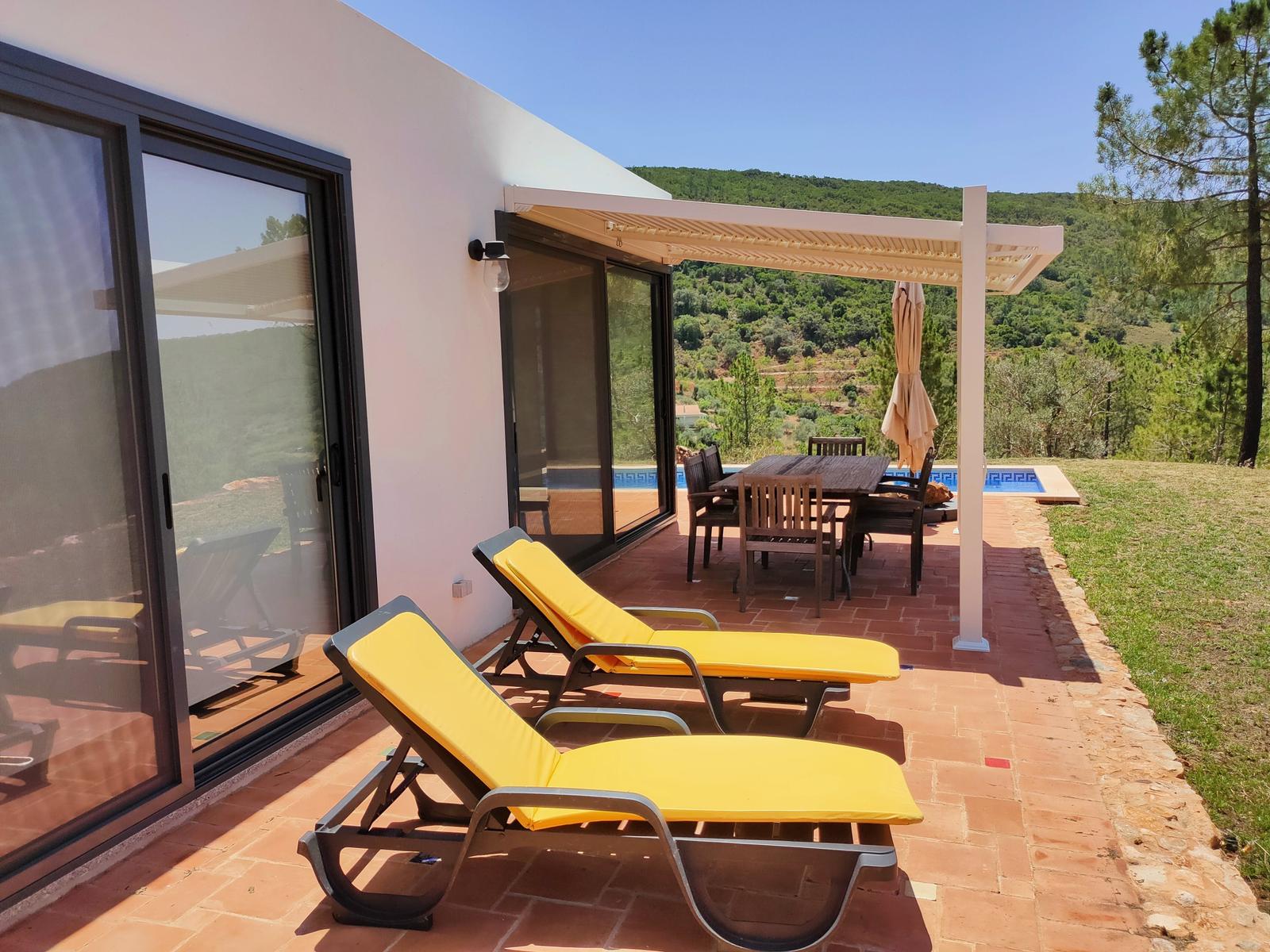 Terrasse mit Liegen, Tisch und Blick auf Pool und Hügel.