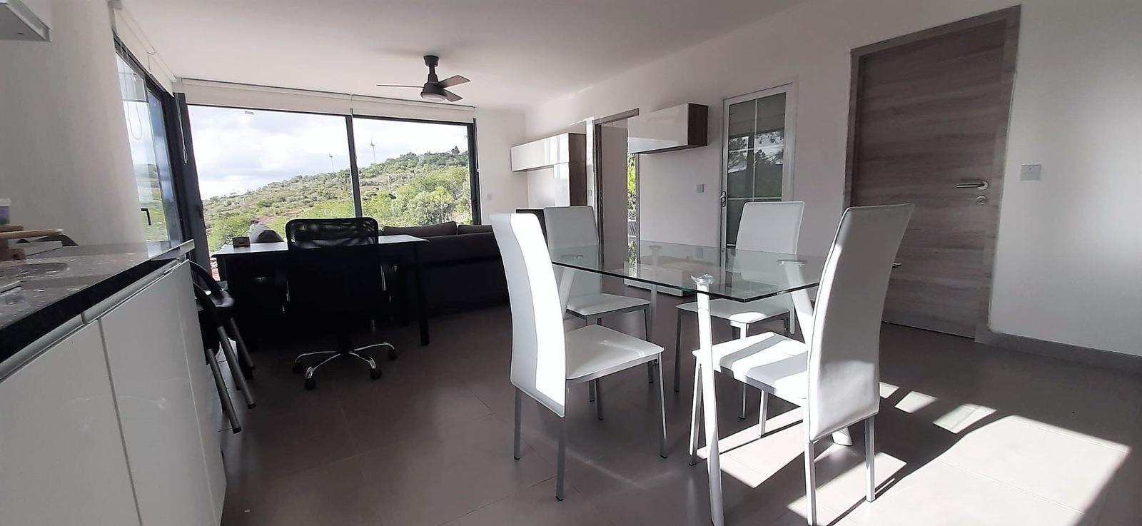 Essbereich mit Glas-tisch und weißen Stühlen. Wohnbereich mit Sofa und Aussicht.