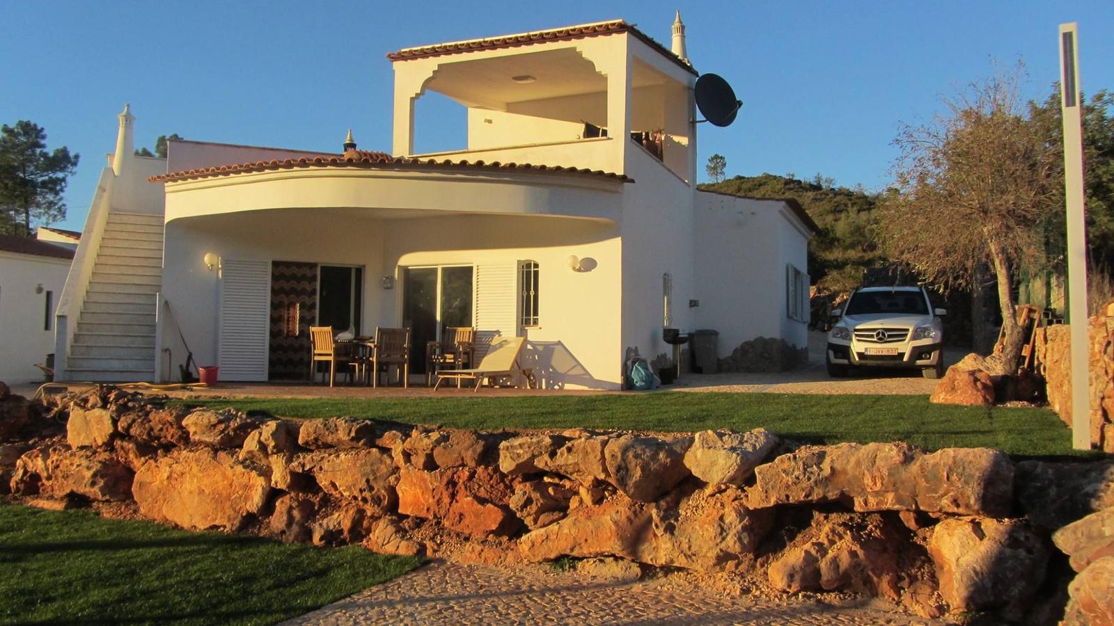 Wohnhaus mit Terrasse, Garten und Steinmauer. Ein Auto parkt vor dem Haus.