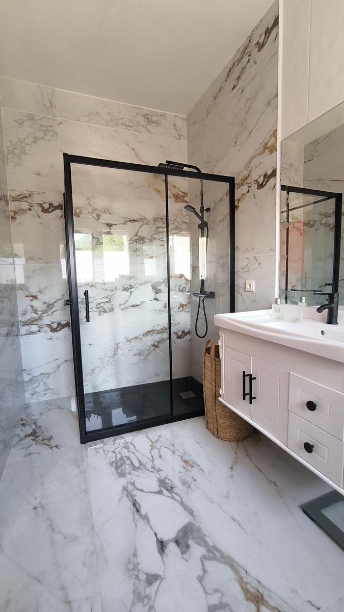Badezimmer mit marbliertem Boden und Wand, Dusche mit Glaswand und Waschtisch mit Spiegel.