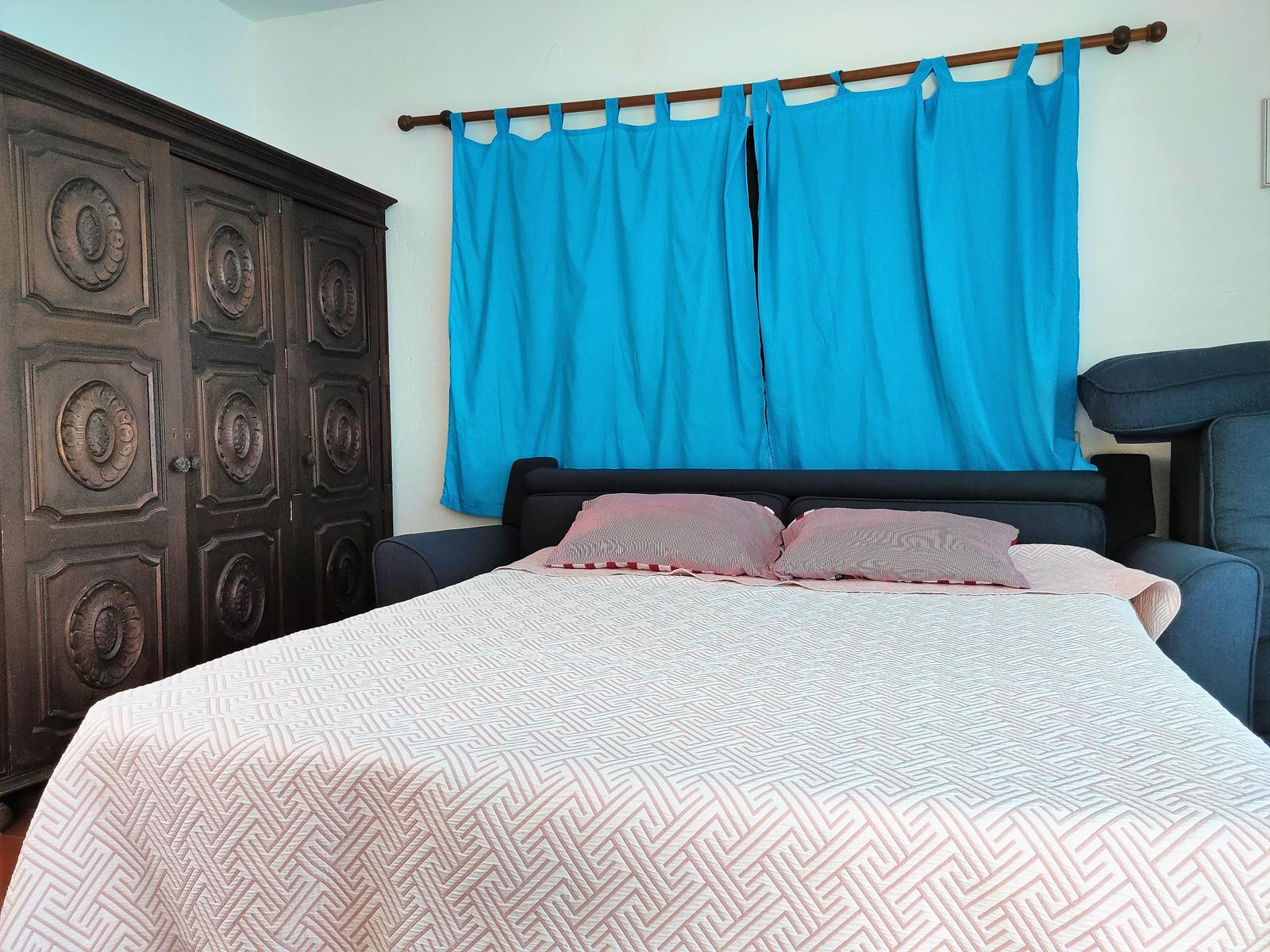 Schlafzimmer mit Bett, dunklem Schrank und blauen Vorhängen.