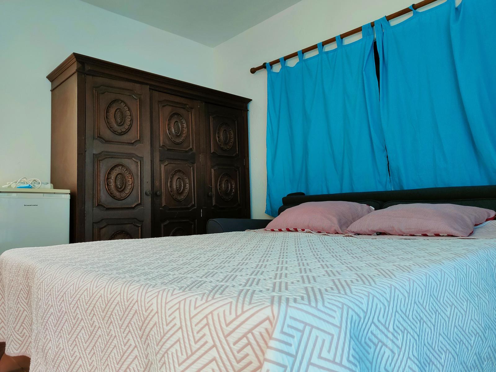 Schlafzimmer mit Bett, Holzschrank und blauen Vorhängen.