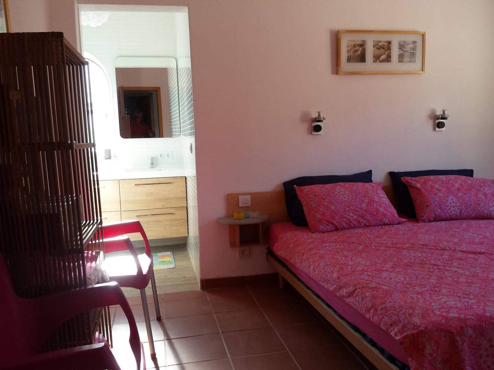 Schlafzimmer mit Bett, Wandbild und Sicht auf Badezimmer.