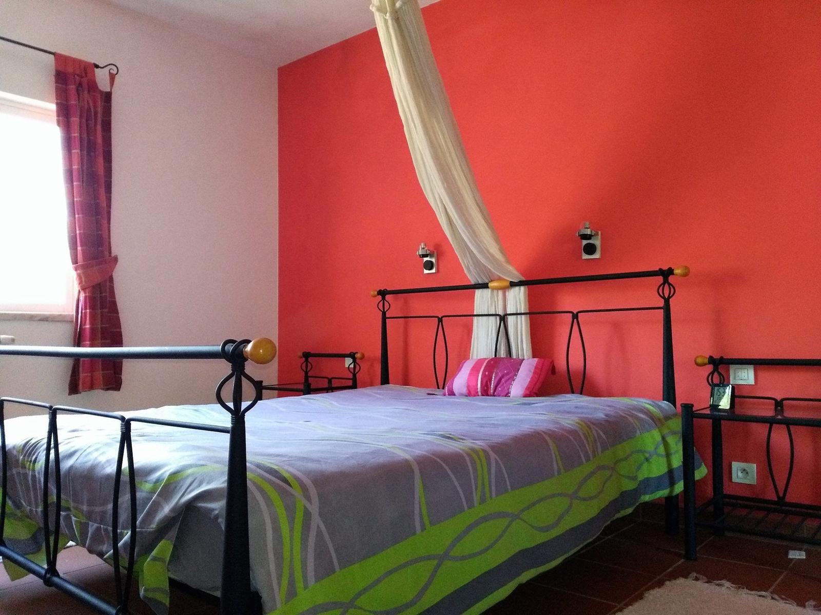 Schlafzimmer mit roter Wand, Metallbett und Vorhängen