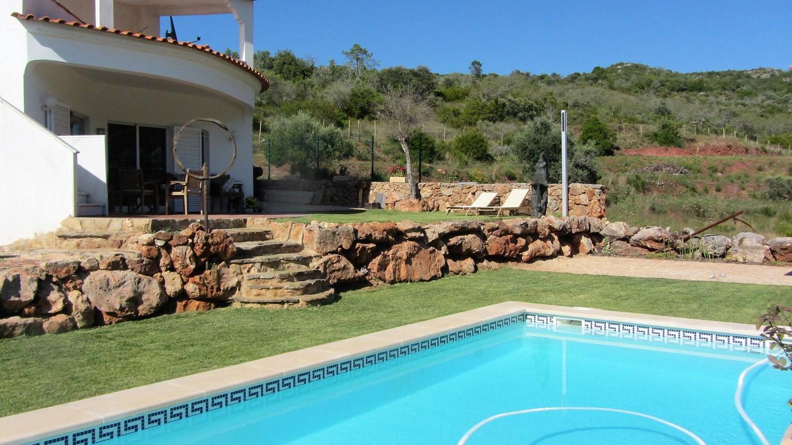 Pool mit Steinmauer, Terrasse und Garten im Hintergrund.
