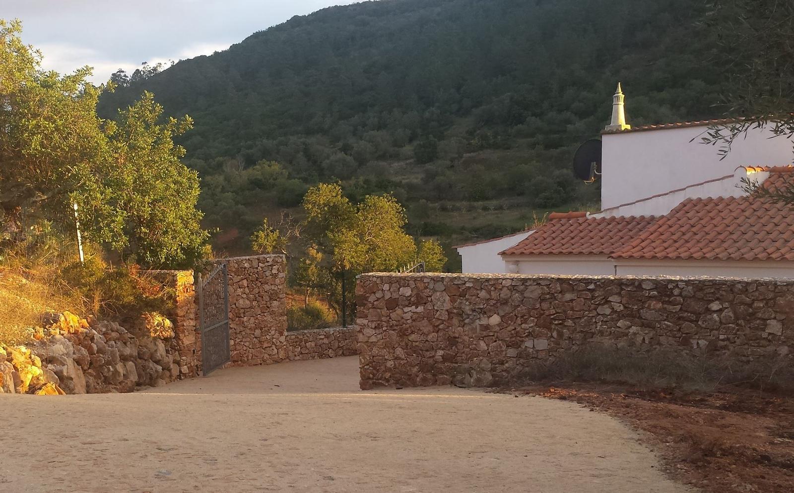 Eingangstor zu einer Villa mit Steinmauer und Berg im Hintergrund.