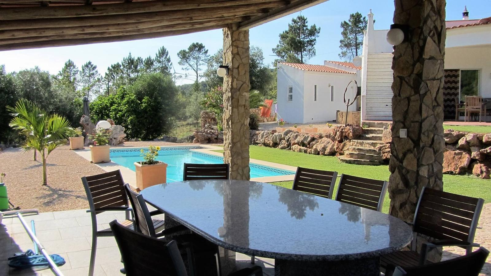 Terrasse mit Tisch und Stühlen, Pool und Garten im Hintergrund.