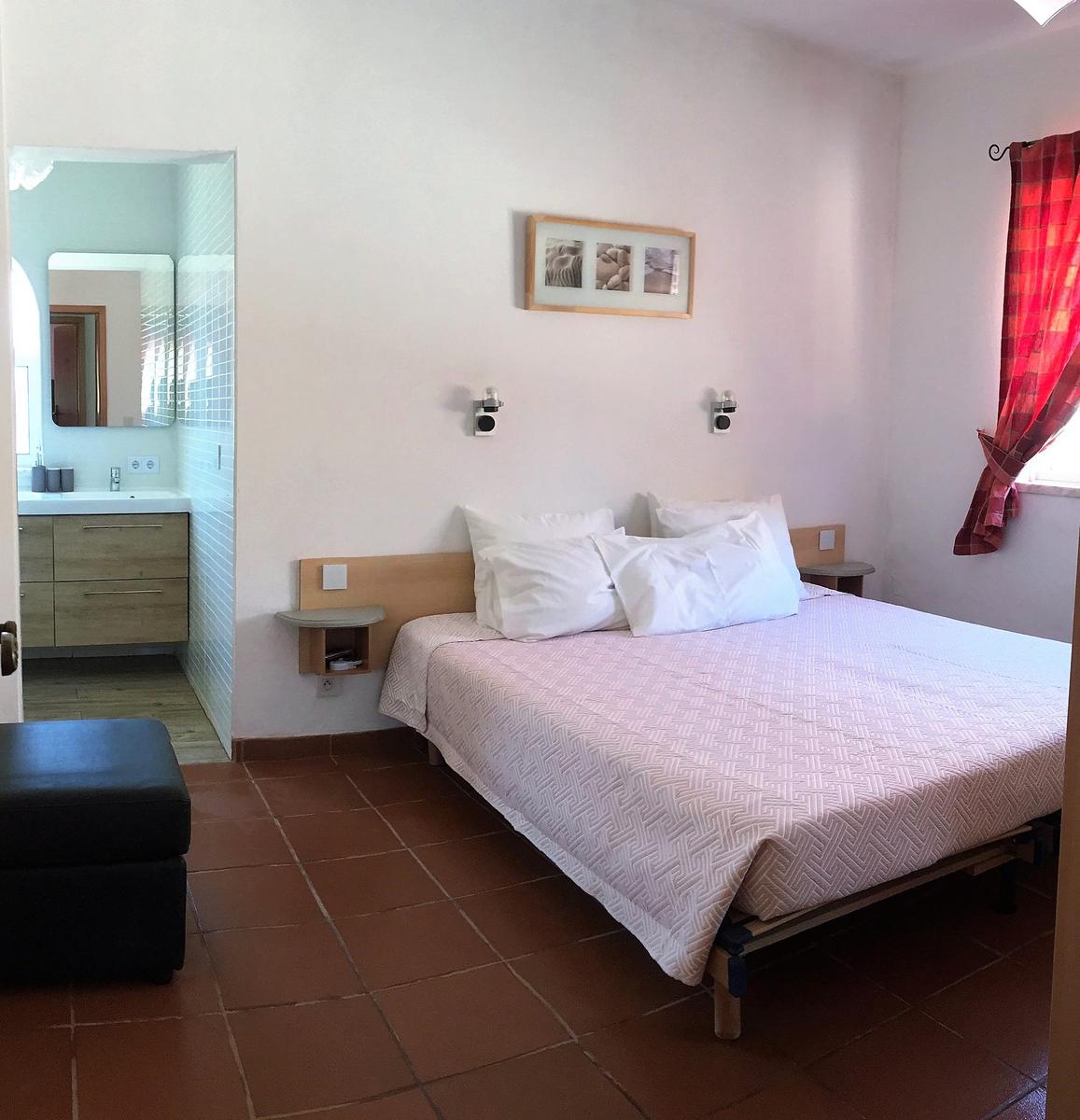 Schlafzimmer mit Doppelbett, Bad und Fenster mit rotem Vorhang.