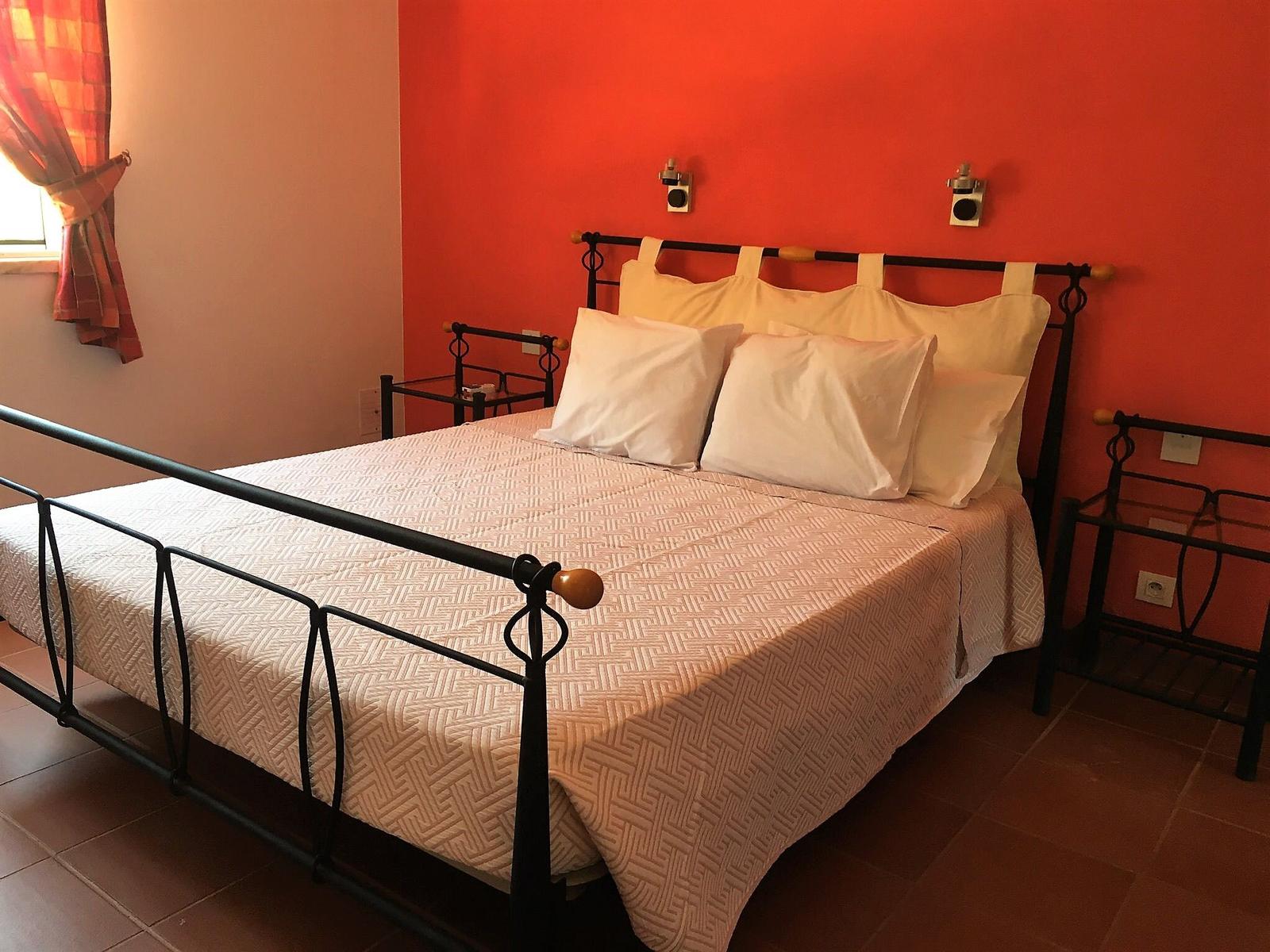 Schlafzimmer mit Bett, roter Wand und Fenster mit Vorhängen