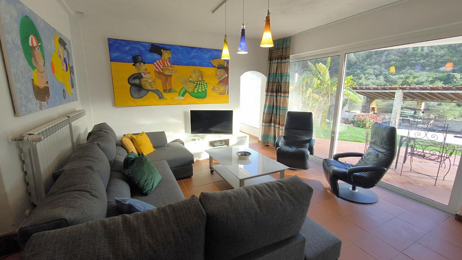 Wohnzimmer mit Sofa, Fernseher und Blick auf Terrasse