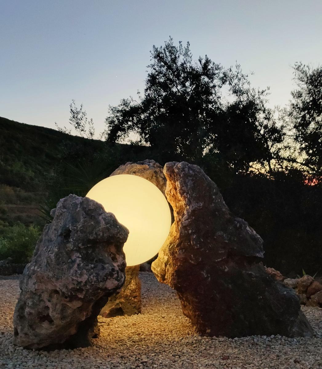 Eine leuchtende Kugel zwischen zwei Felsen im Garten bei Sonnenuntergang.