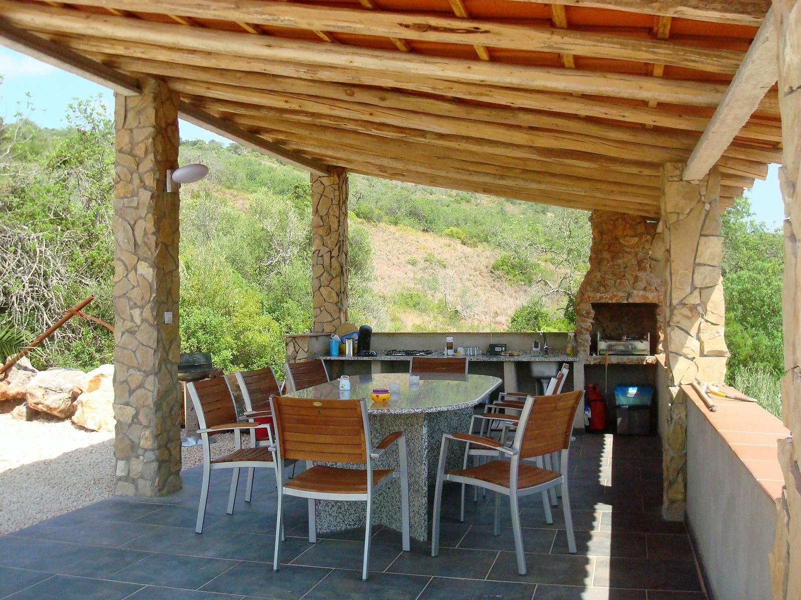 Außenbereich mit Tisch, Stühlen und Grillplatz. Steinpfeiler und Holzdecke.