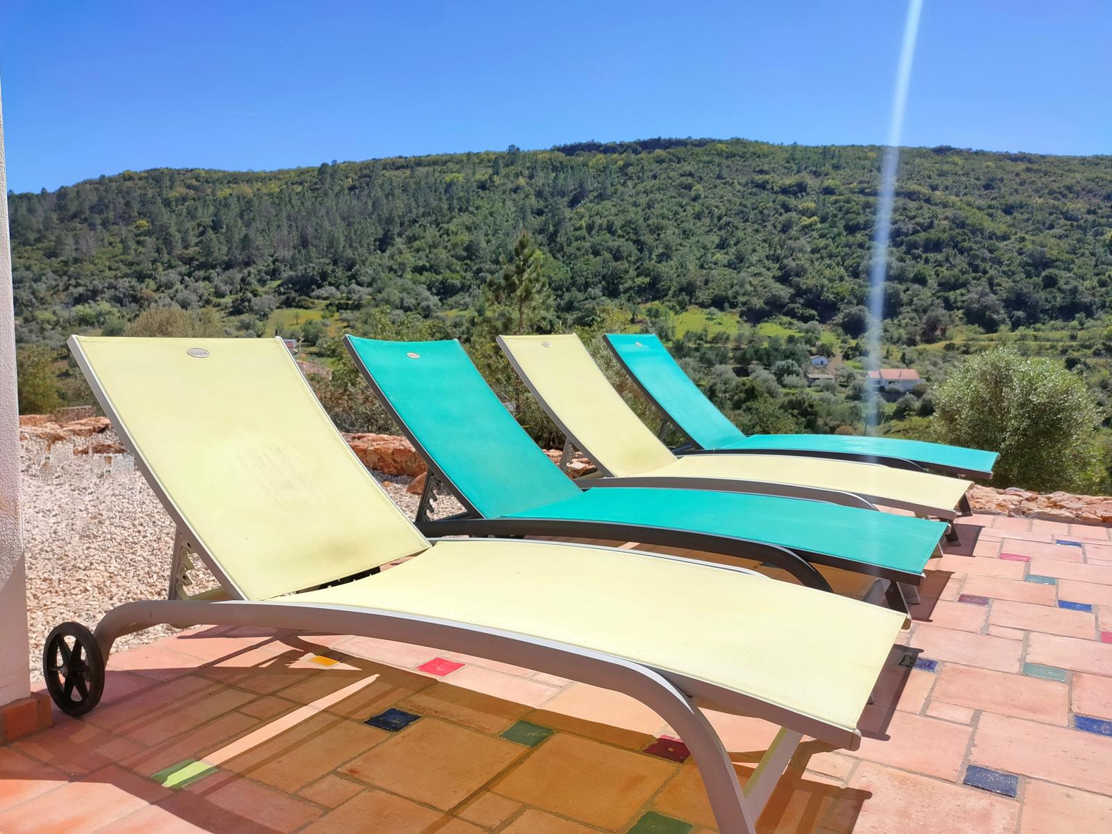 Terrasse mit Liegestühlen und Blick auf grüne Hügel.