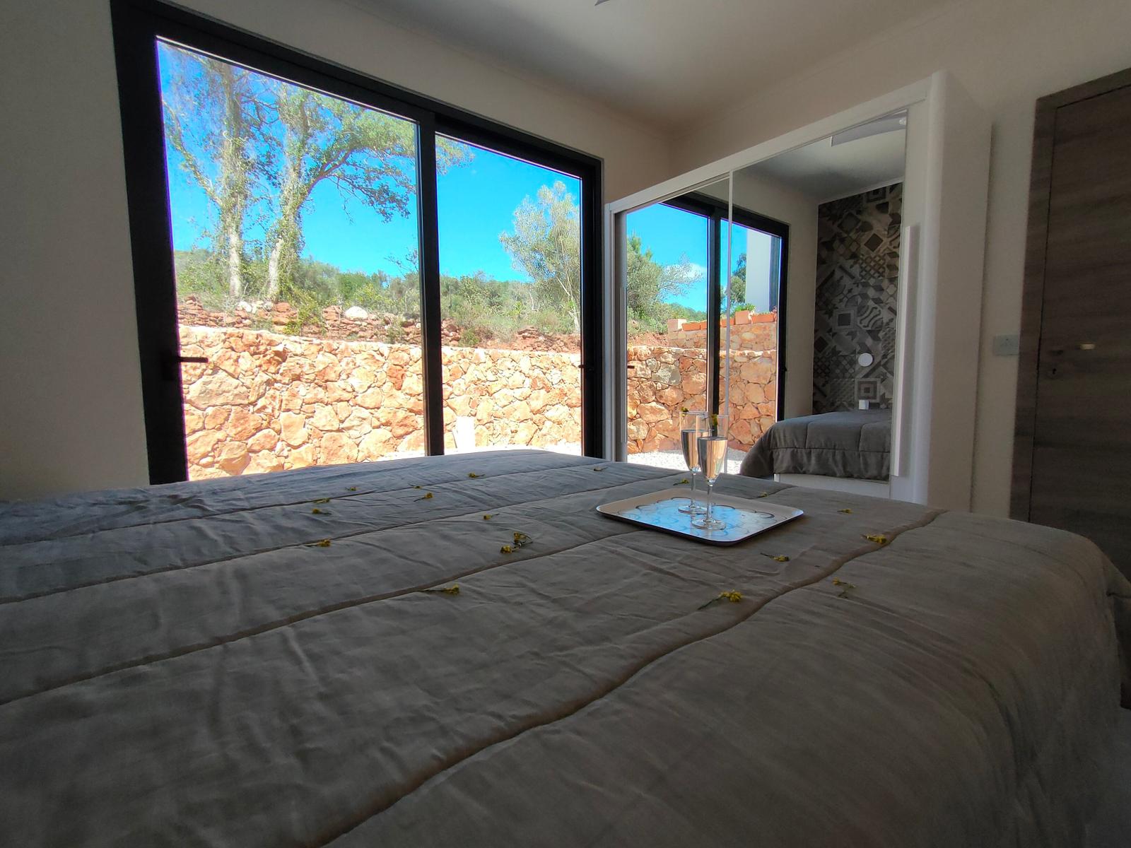 Schlafzimmer mit großem Fenster und Blick auf Steinmauer und Bäume