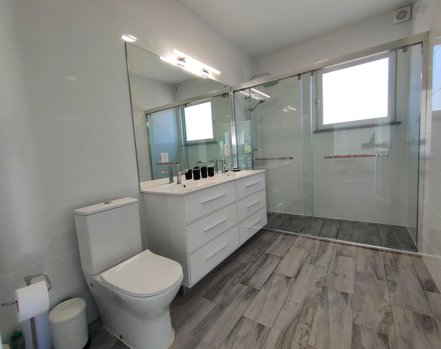 Badezimmer mit Dusche, Waschbecken und Toilette. Holzoptik Boden.