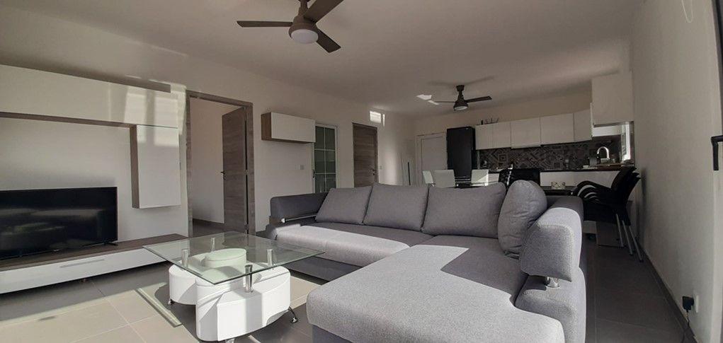 Wohnbereich mit Sofa, Couchtisch und Fernseher. Küche im Hintergrund.