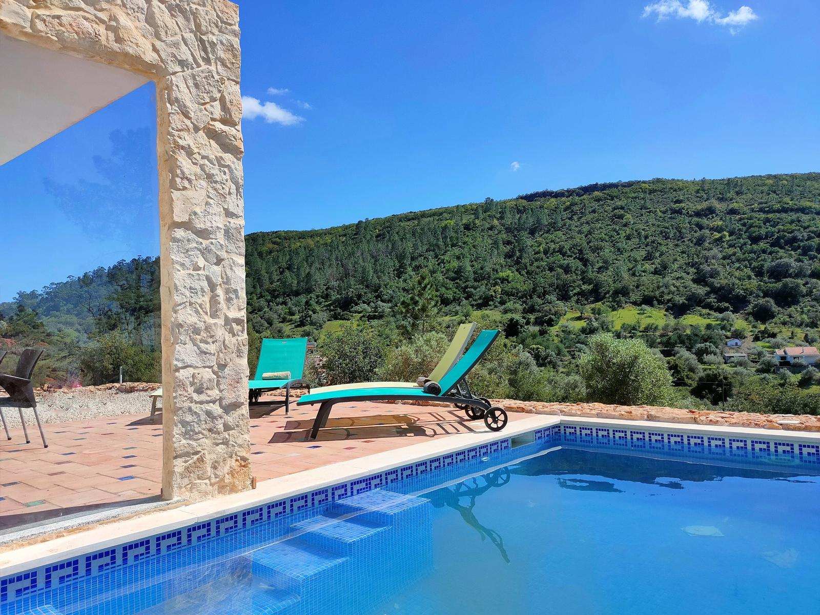 Pool mit Liegestühlen und Blick auf bewaldete Hügel.