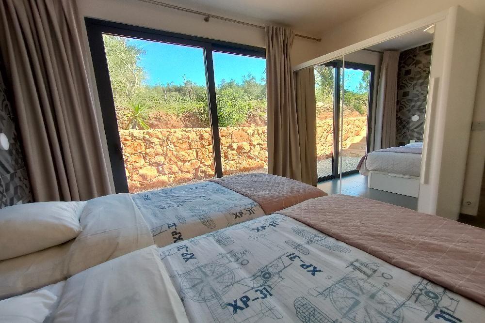 Schlafzimmer mit Doppelbett und Blick auf Steinmauer und Grünflächen.