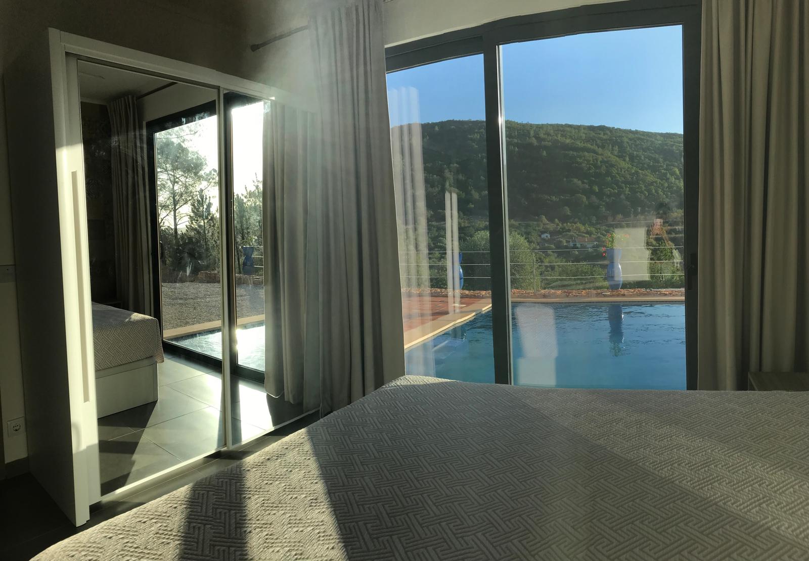 Schlafzimmer mit Blick auf Pool und Berglandschaft durch große Glasflächen.