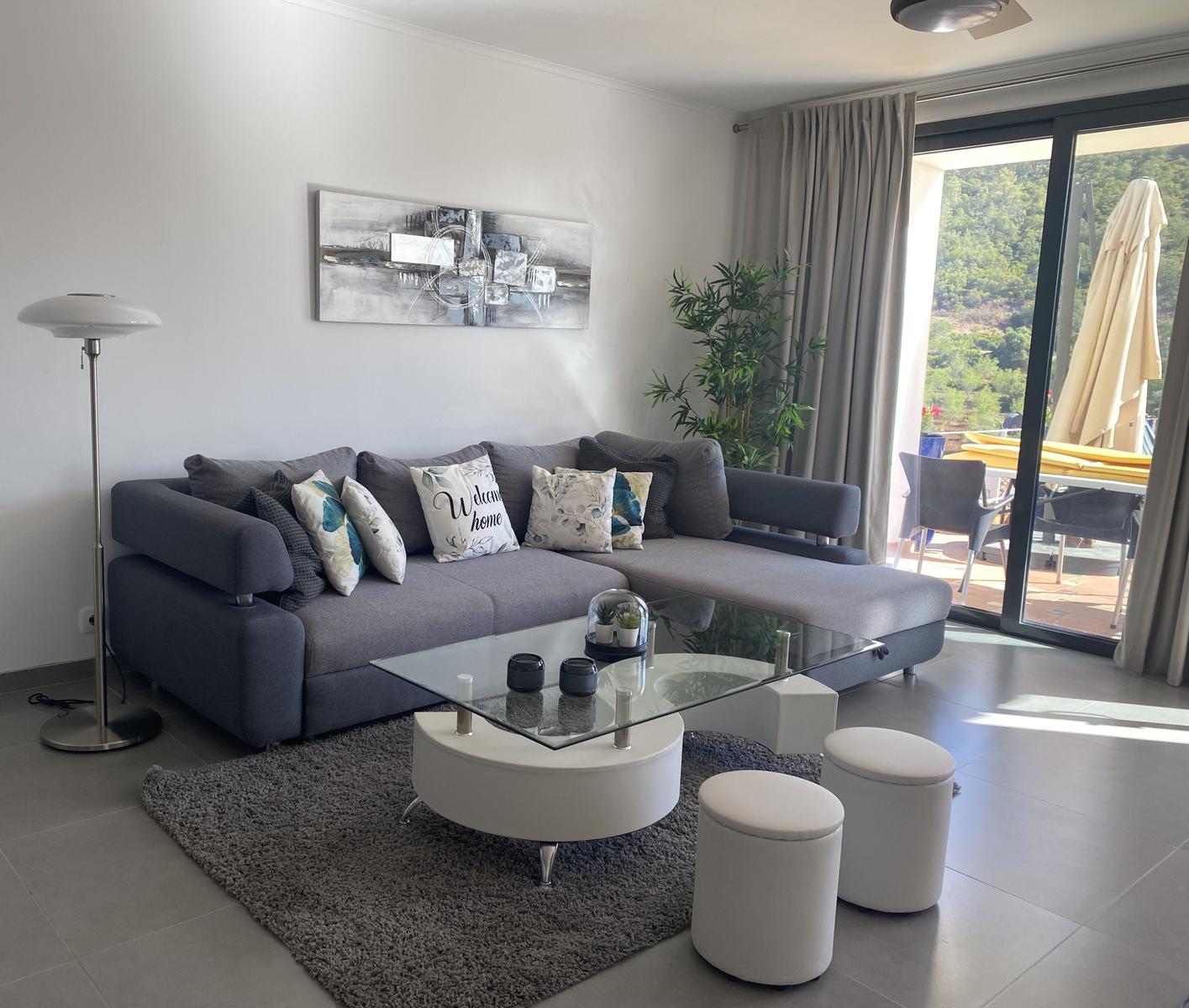 Wohnzimmer mit grauem Sofa, Glas-Tisch und Blick auf Balkon.