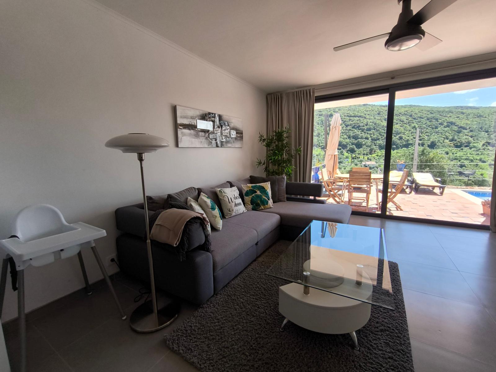 Wohnzimmer mit Sofa, Couchtisch und Blick auf Balkon mit Pool.