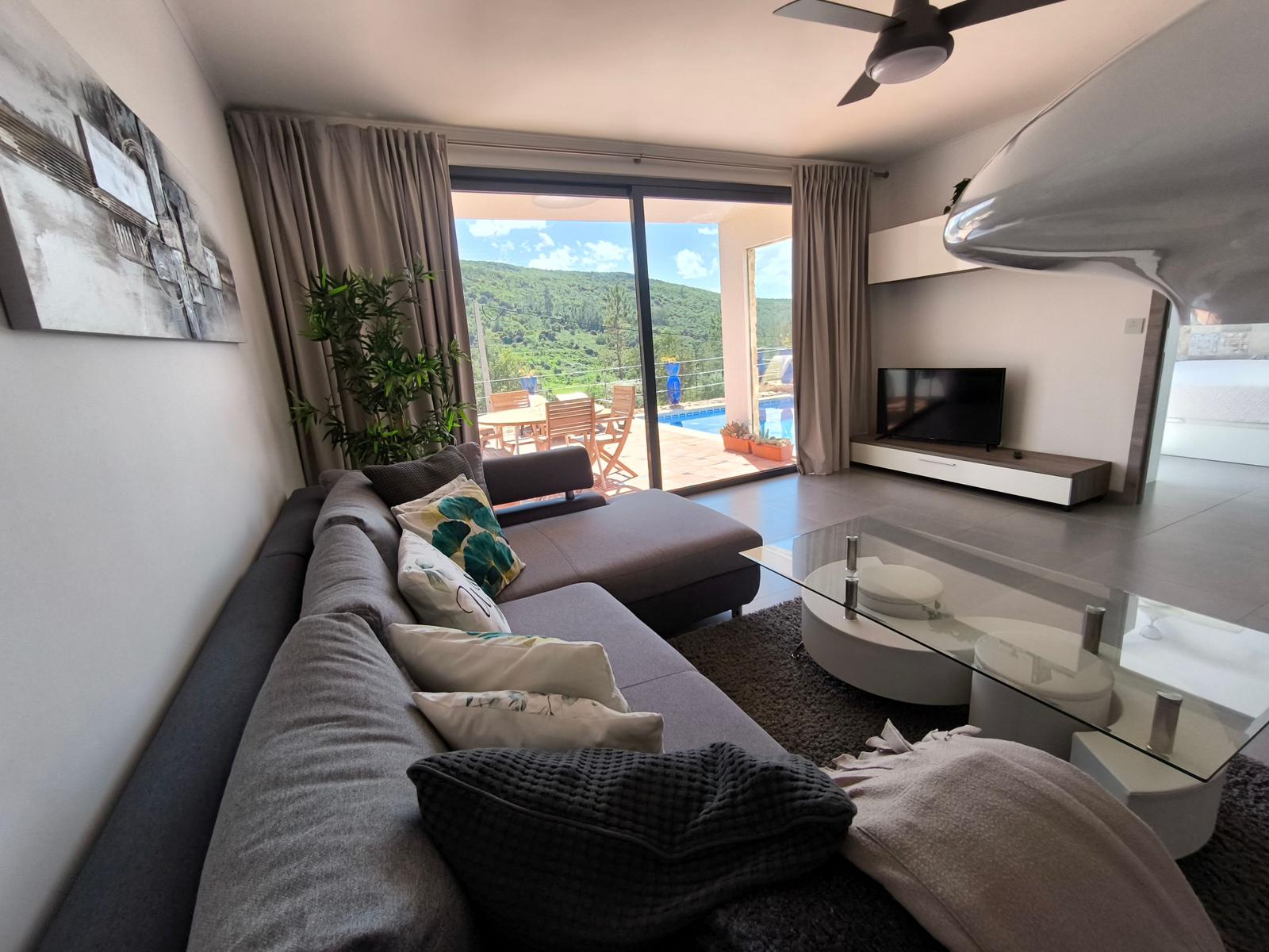 Wohnzimmer mit Sofa, Glas-Tisch und Blick auf Pool und Garten
