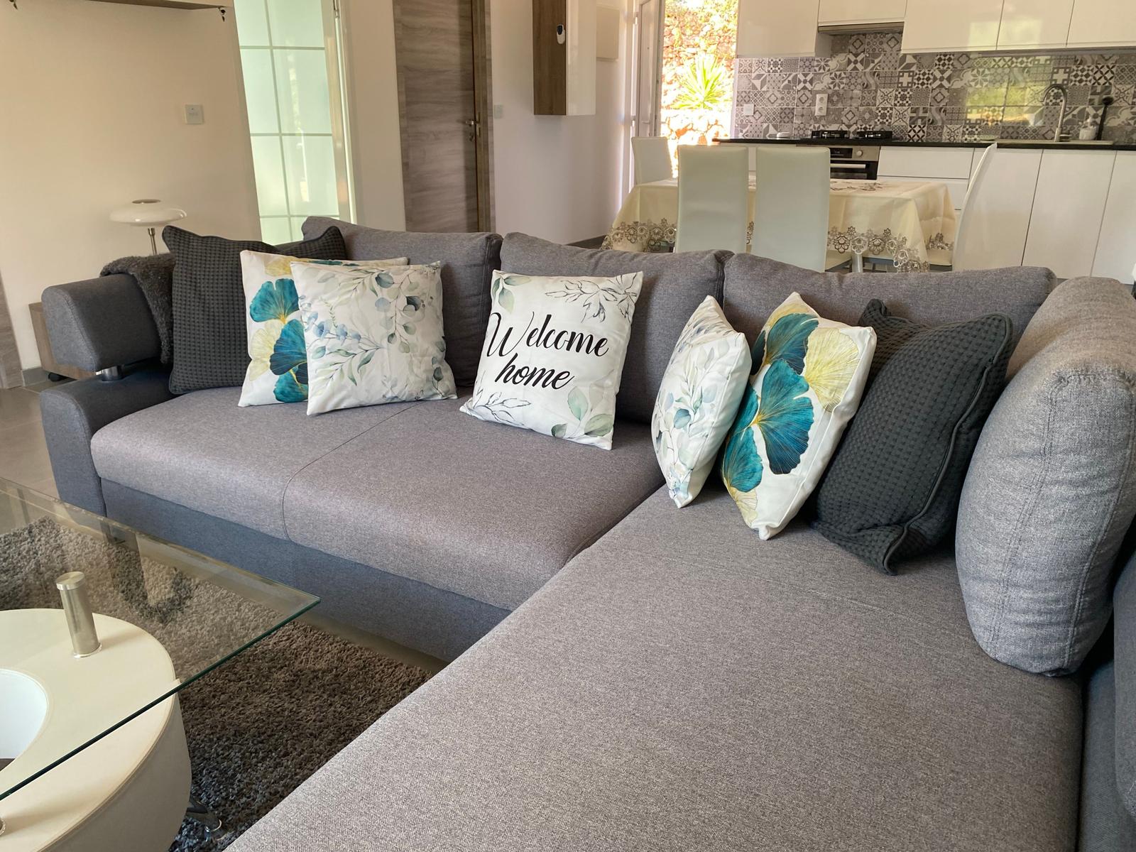 Großer grauer Sofa mit Kissen im Wohnbereich. Küche und Essbereich sind sichtbar.