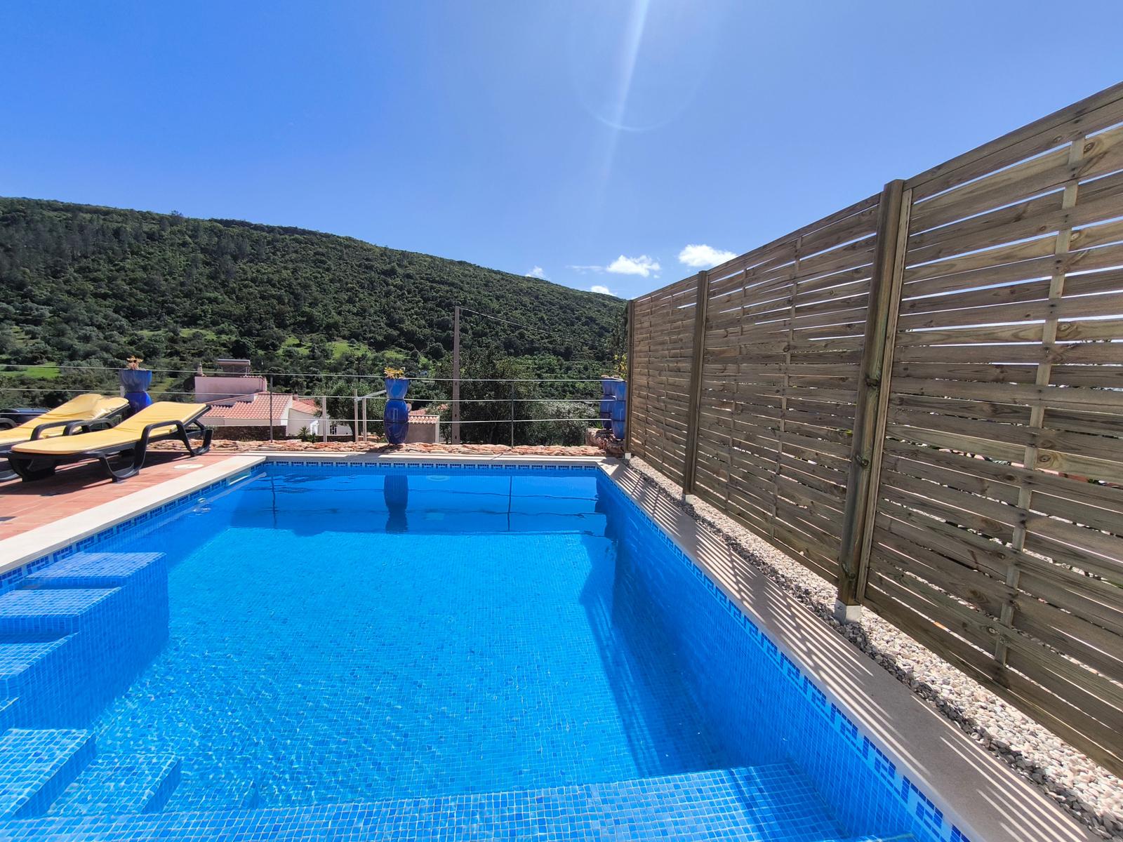 Pool mit Liegestühlen und Holzzaun. Berglandschaft im Hintergrund.