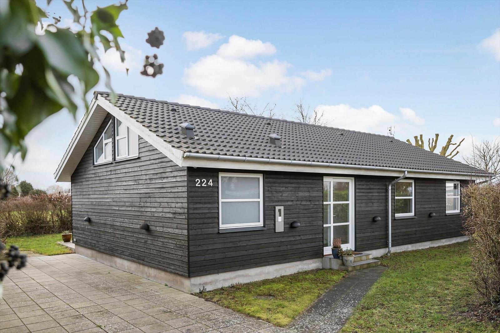 Ein kleines Haus mit dunkler Fassade und weißen Fenstern. Die Tür ist weiß und mit Pflanzen geschmückt.