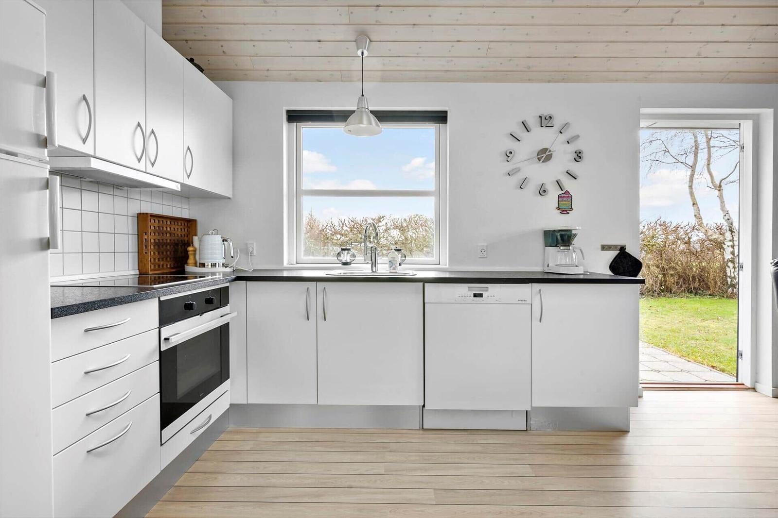 Moderne Küche mit weißen Schränken, schwarzer Arbeitsplatte und Blick auf Garten.