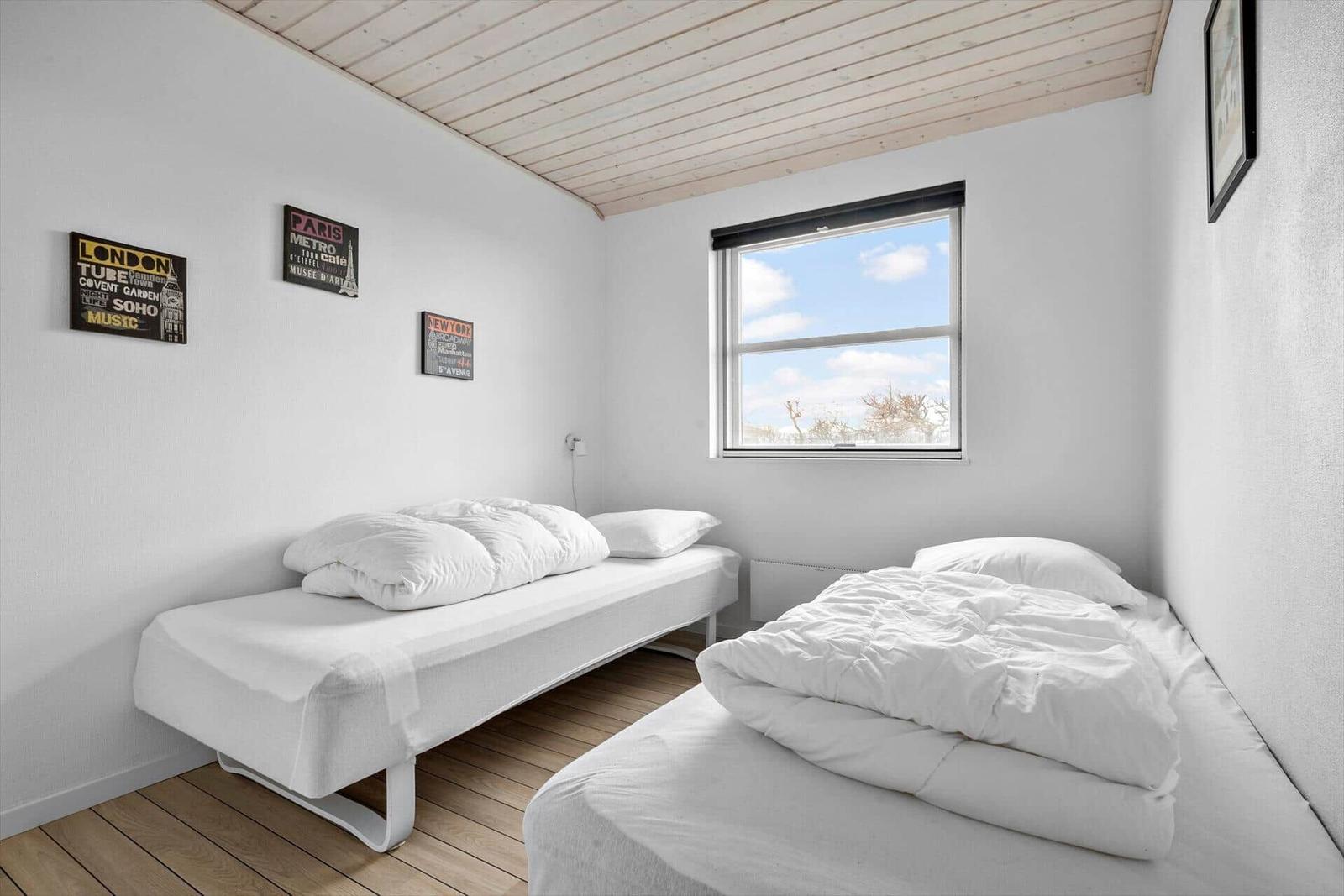 Zwei Betten mit weißen Bettwäschen, Fenster mit Blick draußen, Holzboden und Wanddekoration.