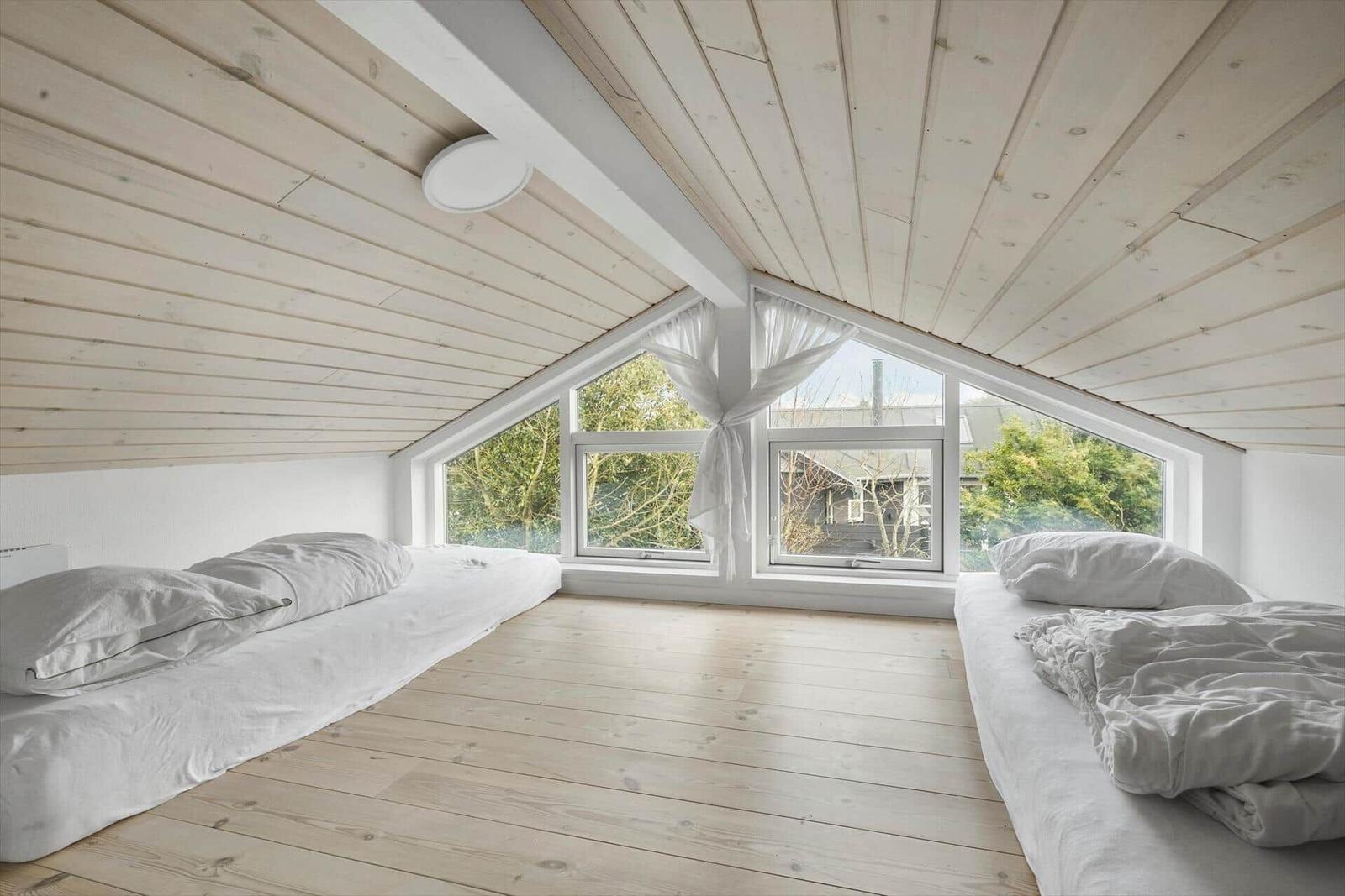 Zwei Betten unter einem Holzdach mit großem Fensterblick auf Bäume