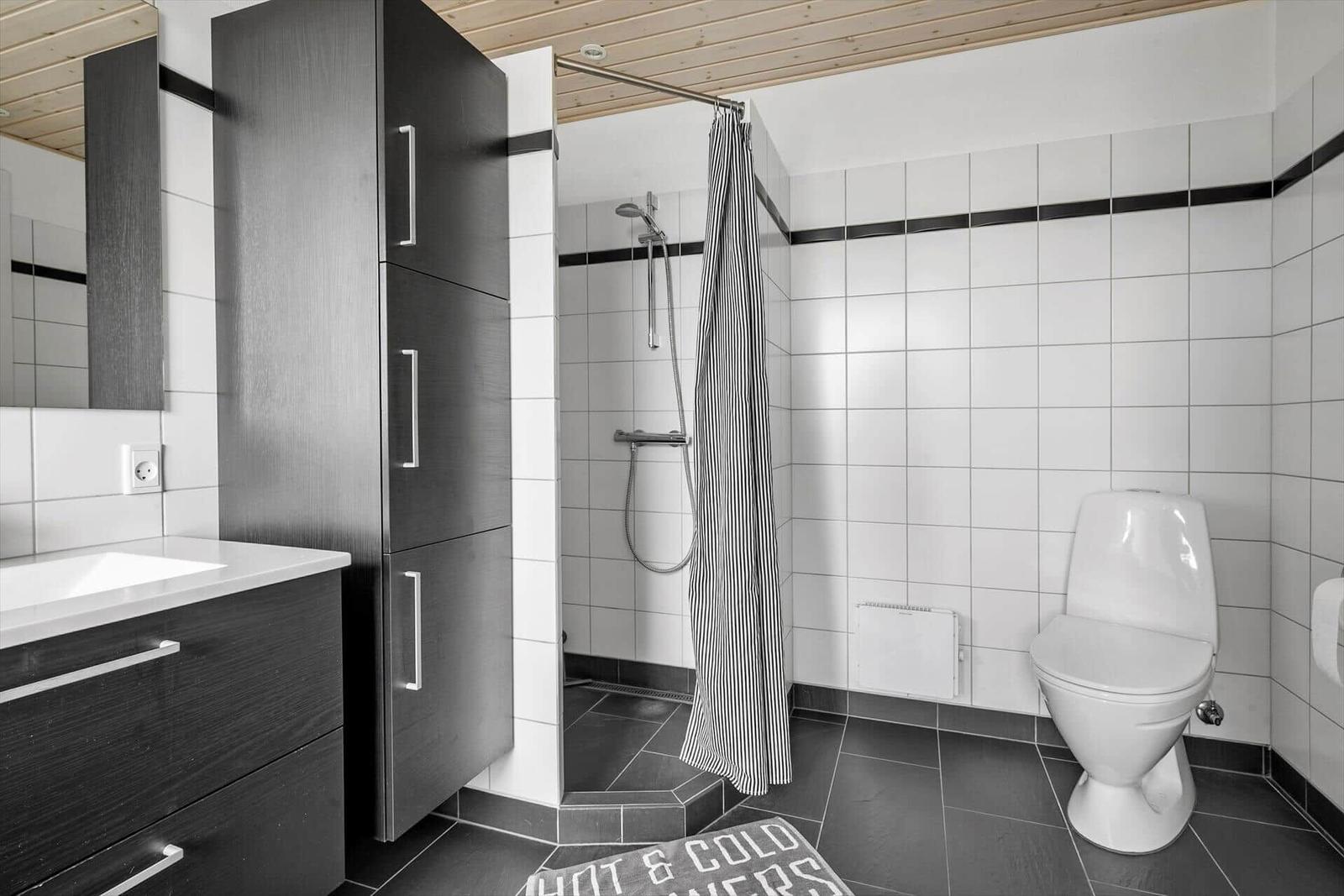 Badezimmer mit Dusche, Toilette und Waschbecken. Weiße Fliesen und dunkler Holzboden.