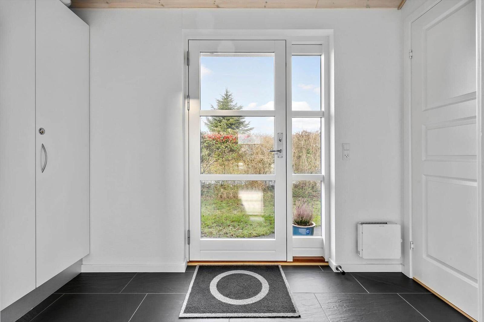 Eingangsbereich mit weißer Tür, schwarzen Fliesen und Blick auf Garten.