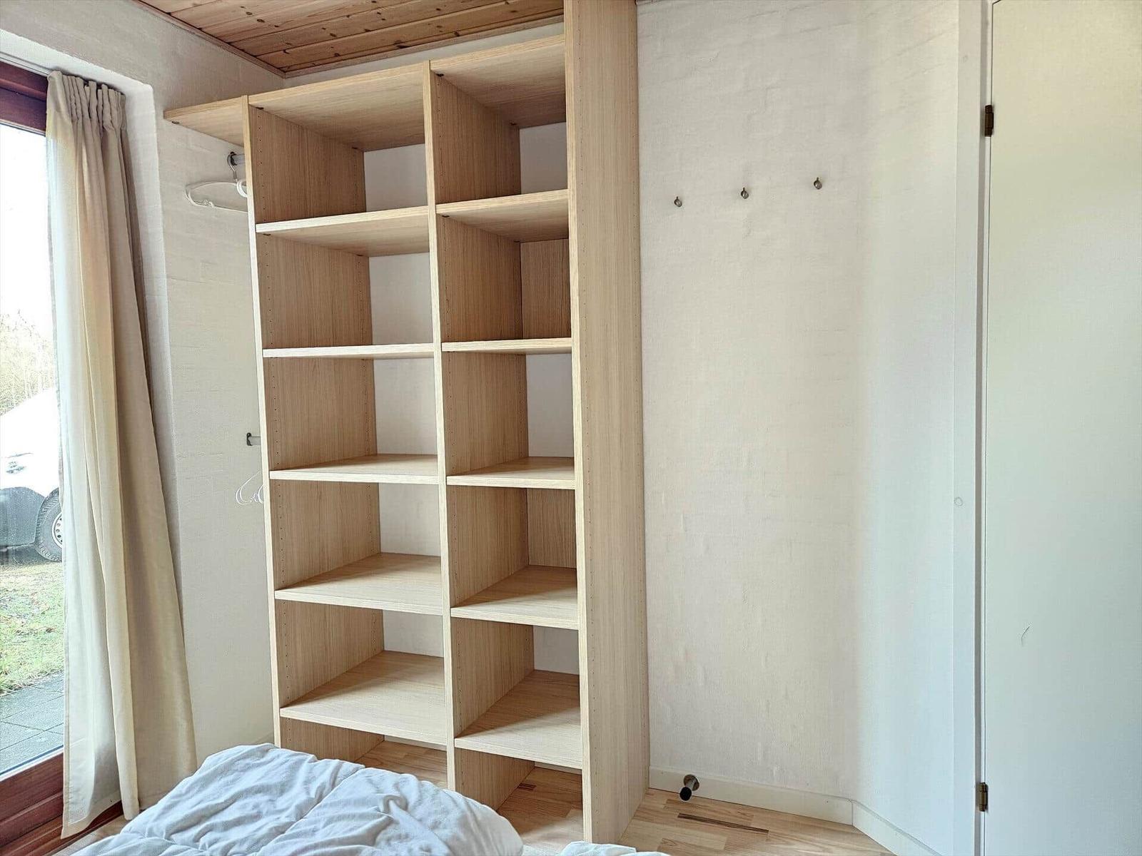 Schlafzimmer mit Holzregal, Fenster und Bett. Wand mit Haken.