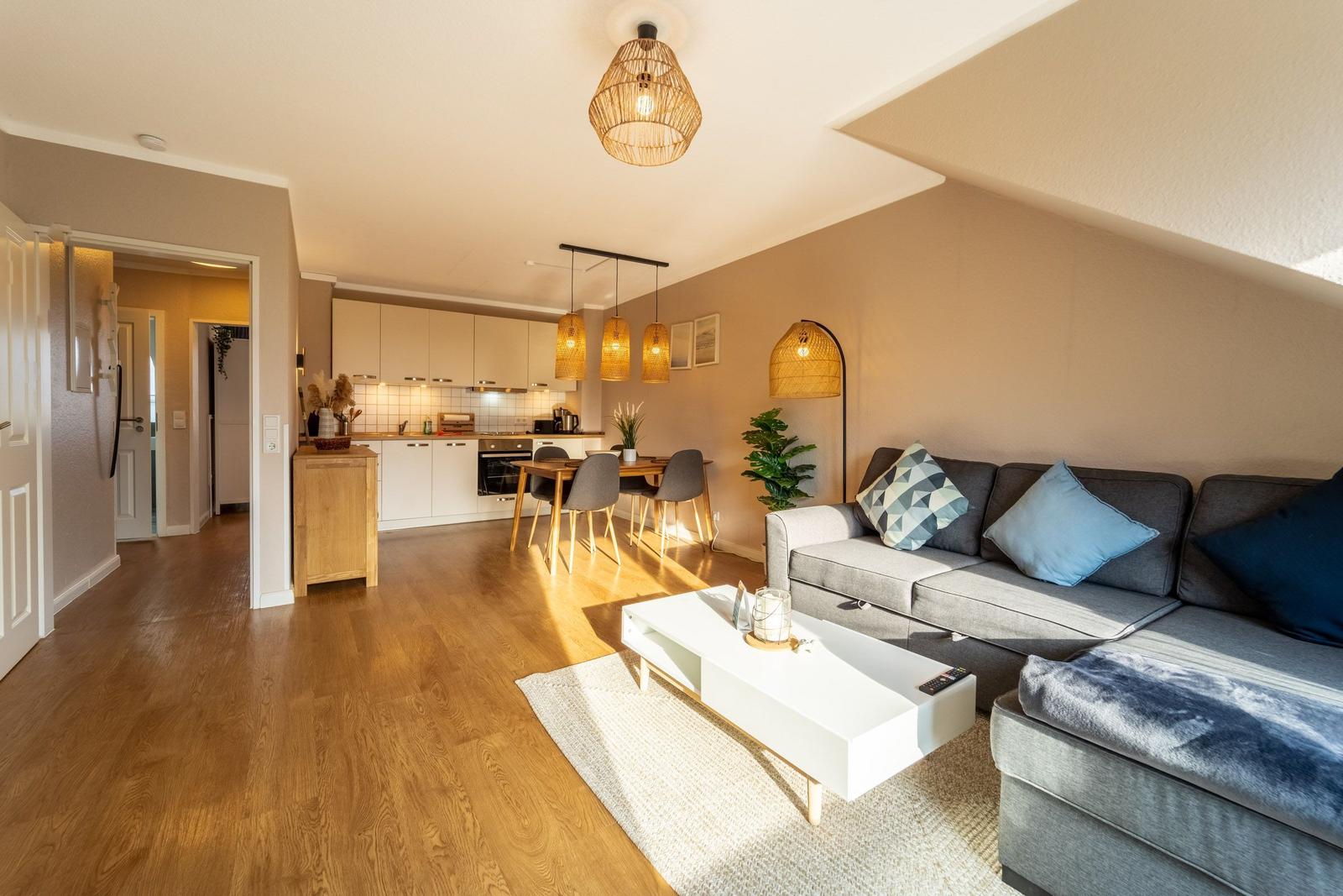 Wohn- und Essbereich mit Küche unter Dachschrägen. Holzboden, Sofa, Couchtisch und Pendelleuchten.