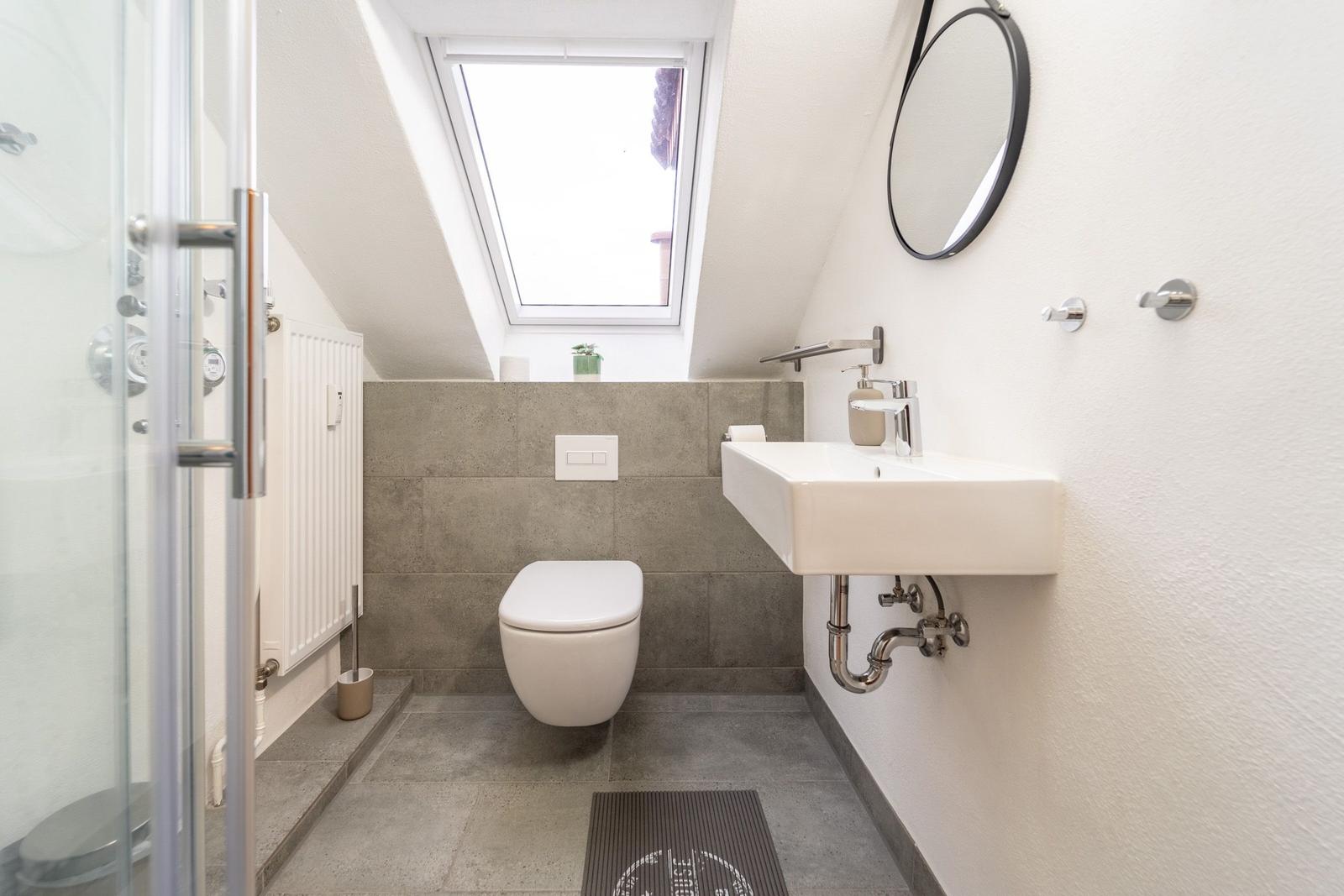 Badezimmer mit Dusche, Toilette und Waschbecken unter Dachschrägen.