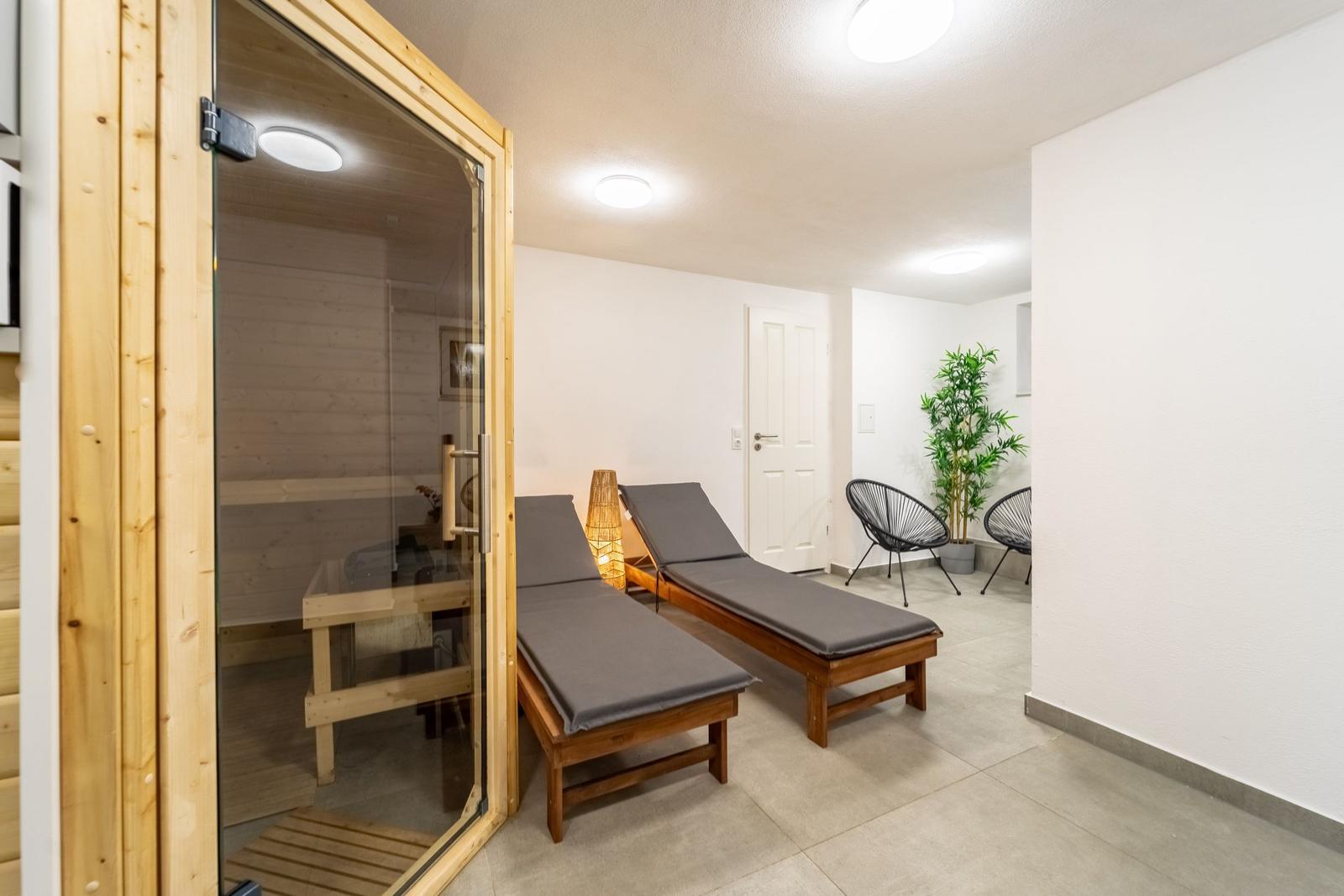 Sauna mit Glasfront, zwei Liegen und Pflanze im Raum.