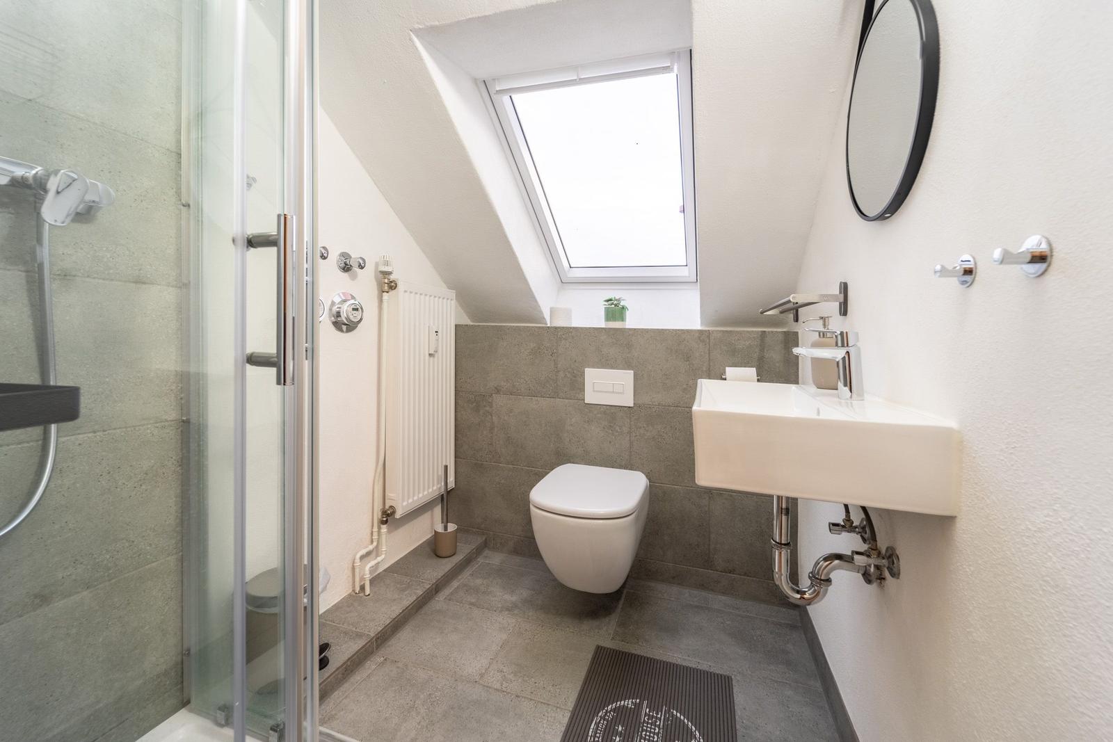 Dusche, Toilette und Waschbecken unter Dachschräge mit Dachfenster.