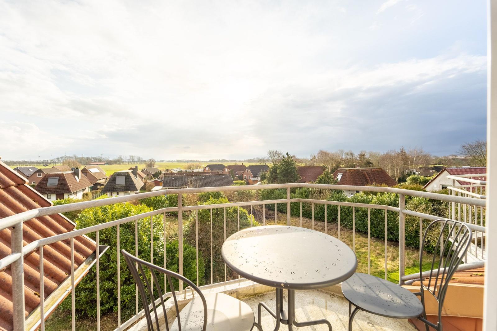 Balkon mit Tisch und Stühlen. Blick auf Dächer und Grünflächen.