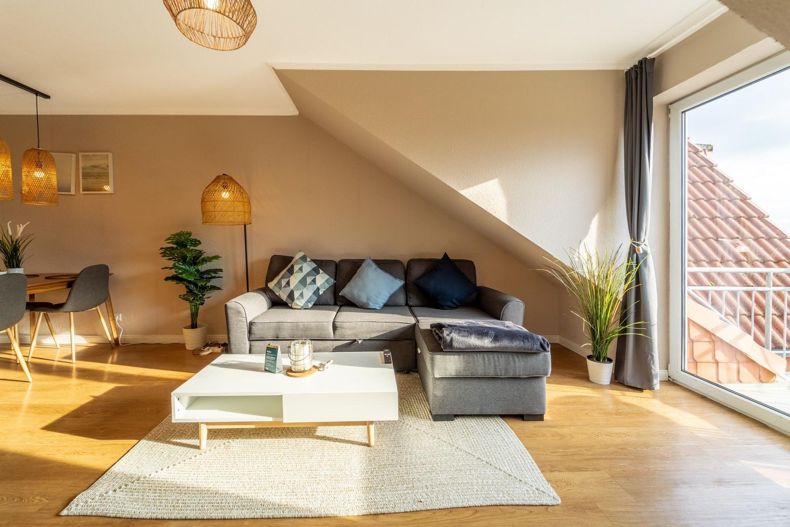 Wohnzimmer mit Sofa, Couchtisch und Balkon. Holzboden und schräge Decke.